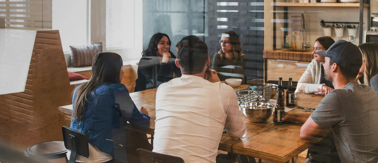 Eine Gruppe von Menschen sitzt entspannt an einem Holztisch in einem modernen Büro und unterhält sich.